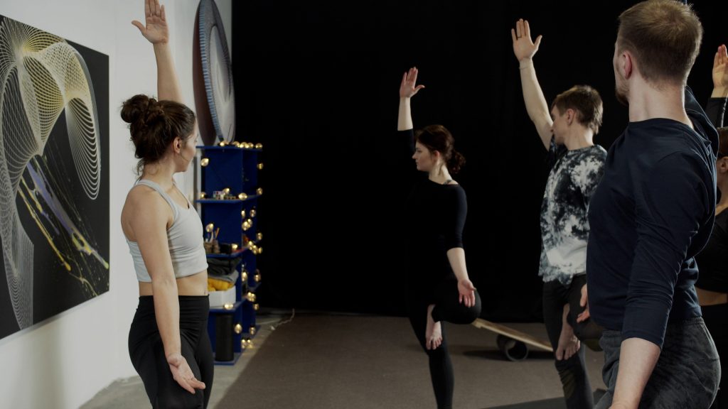 Group of slim people standing on one leg while doing yoga in studio